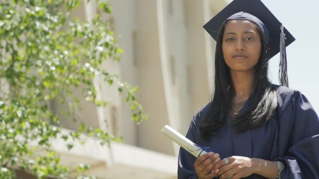 Portrait of a confident young Indian woman wearing her high school graduation cap and gown holding her diploma