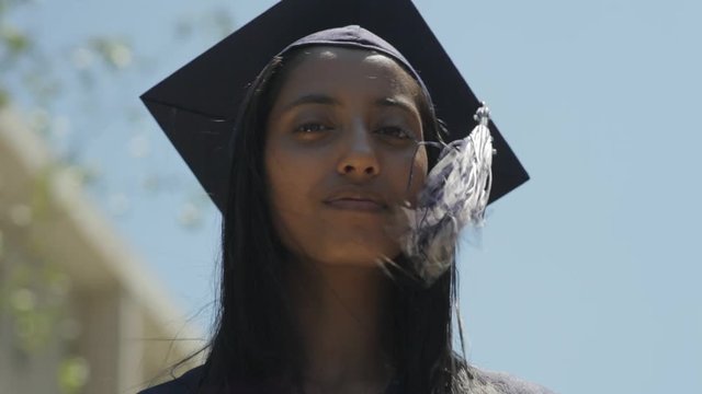 Confident young Indian woman wearing her high school graduation cap and gown receives her diploma and shakes the principal's hand   