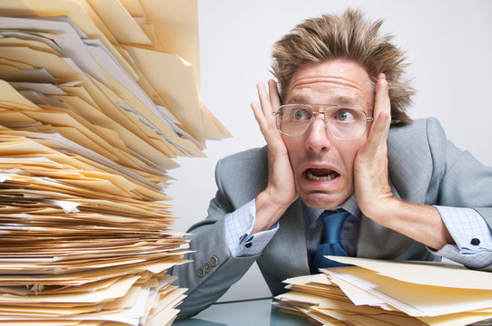 Stressed office worker looking with   shock at a massive stack of file folders on his desk