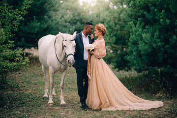 Newlyweds are standing near a white horse in nature, full height portrait