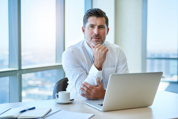 Handsome mature businessman with laptop in office looking serious - obrazy, fototapety, plakaty