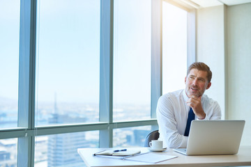 Mature businessman in office looking away optimistically, with sunflare - obrazy, fototapety, plakaty