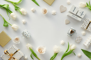 Valentines day flat lay, top view on white background with fresh tulip flowers, coffee cups, Valentine gift in white paper with golden lines, marshmallows. Wood calendar with 14 February, copy-space.