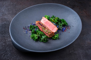 Traditionelles gegrilltes dry aged Wagyu Rinderhüften Steak aufgeschnitten mit Kalette und Kräuter als closeup auf einem Modern Design Teller mit Textfreiraum