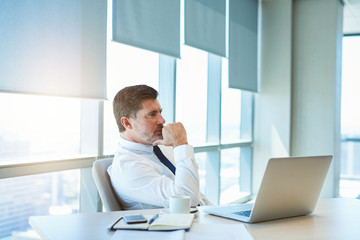Mature business manager sitting thinking at his desk