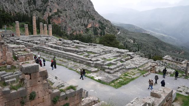 Delphi, Grece, Europe - dicember 30 2019: turists visit the ruins of the ancient temple of Apollo, archaeological site of Delphi along the slope of Mount Parnassus, UNESCO World Heritage, Greece.