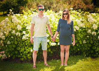 Fototapeta premium Handsome man and his beautiful pregnant wife hugging and smiling for a walk in the park