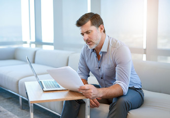 Mature man with laptop and paperwork in a business lounge