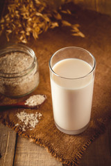Glass of oat milk on a wooden background. Lactose-free vegetable diet milk. Gluten free oat drink on a brown wooden background.