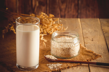 Glass of oat milk on a wooden background. Lactose-free vegetable diet milk. Gluten free oat drink on a brown wooden background.