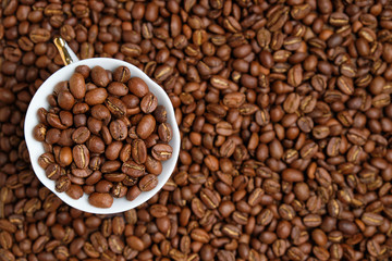 A white cup is peppered with beans against the background of coffee beans. Copy space. Top view.