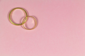 Two wedding rings in gold on pink background