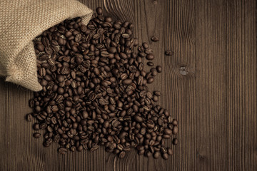 Coffee beans falling out of a wicker bag against a wooden background.