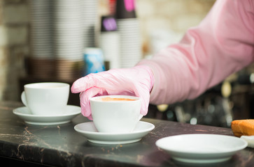 bartender in pink glove putting fresh coffee in cup on table