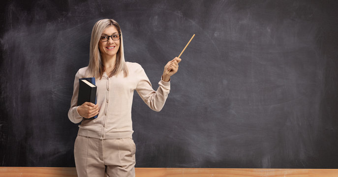 Female teacher standing in front of a blackboard and pointing with a stick