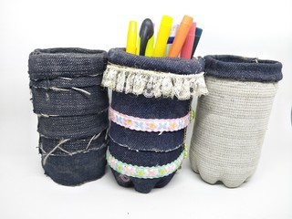 Handmade craft recycle bottle and jeans become pencil stationary case desk. Tube box shape with top hole. Decoration with sand, button and bordir  embroidery. Work process cut sewn taped glued dry. 