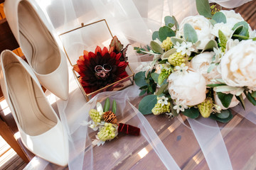 Wedding details. Wedding rings, a beautiful bouquet of white roses and peonies, a boutonniere and bridal shoes are lie on a veil