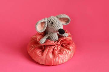 Gray knitted toy mouse sits in a pink silk bag against a pink paper background