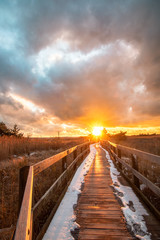 Wooden boardwalk leading towards the sun breaking through dramatic storm clouds. State park in Long Island New York. 