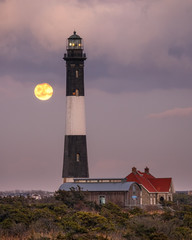 Full moon rising behind a tall stone lighthouse. Fire Island National Seashore, New York. 