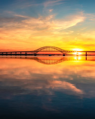  Steel tied arch bridge spanning a bay with crystal clear reflections in the water at sunset. Fire Island Inlet Bridge, part of the Robert Moses Causeway on Long Island New York. 