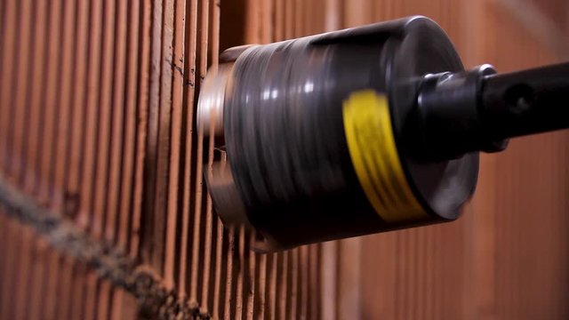 Close up of male with electric drill perforator before making a hole in red brick wall. Stock footage. Worker and professional tool at the construction site.
