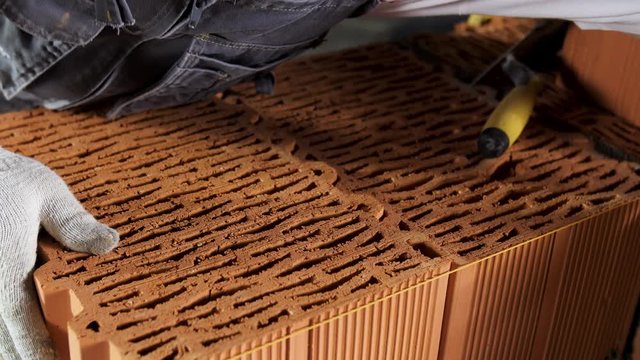 Industrial bricklayer worker placing bricks on cement while building walls. Stock footage. Close up of a man in protective gloves putting heavy brick block to form a layer.