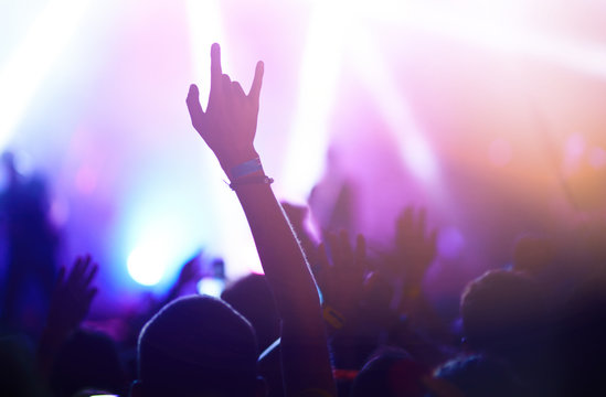 Audience With Hands Raised At A Music Festival And Lights Streaming Down From Above The Stage. Crowd Raising Their Hands, Dancing And Enjoying Great The Concert.