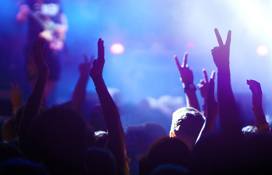 Audience With Hands Raised At A Music Festival And Lights Streaming Down From Above The Stage. Crowd Raising Their Hands, Dancing And Enjoying Great The Concert.