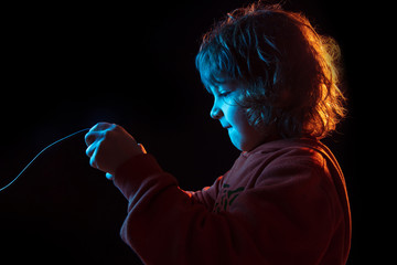 Attented playing videogames. Caucasian boy's portrait on dark studio background in neon light. Beautiful curly model. Concept of human emotions, facial expression, sales, ad, modern tech, gadgets.
