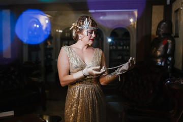 a woman in a golden dress in the image of 20 years old, looks at her hands, on which are long...