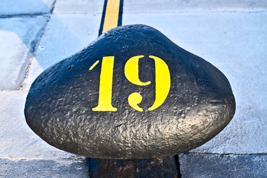 Number 19, nineteen, stencil yellow digit painted on a big commercial harbor bollard.