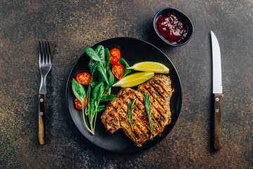 Roasted pork steak on black plate over dark background. With lemon, Cranberry Sauce and wine.