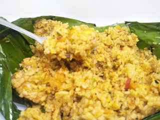 EAT Nasi bakar jawa goreng or grilled rice on banana leaves . Dish is wrapped by using daun pisang then roasted by charcoal. Ingredients serve with seafood, meat, chicken, egg, vegetable, brown color,
