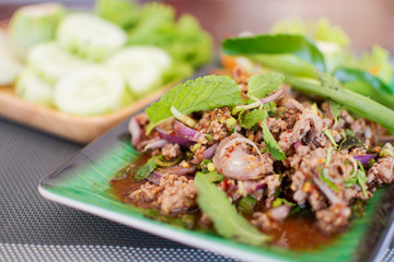 Spicy minced meat salad with blurred cucumbers background, Thai menu