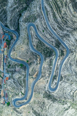 Aerial top down panorama view of a long serpentine curving road going up the hill from the bottom riverbed of the Jucar with dozens of sharp turns drawing an interesting pattern