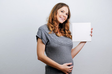 Pregnant young woman holding a blank canvas in her hands. Pregnancy concept, expecting a baby. 