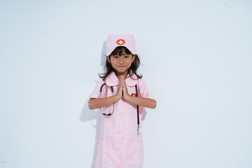 asian little girl wearing doctor uniform with two hands in front of chest is gesture of invite in isolated background