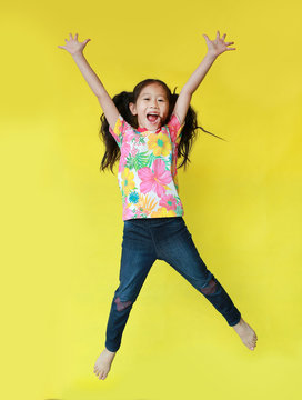 Happy asian little child girl wearing a floral pattern summer dress jumping and freedom movement on air isolated on yellow background. Holiday and summer fashion concept.