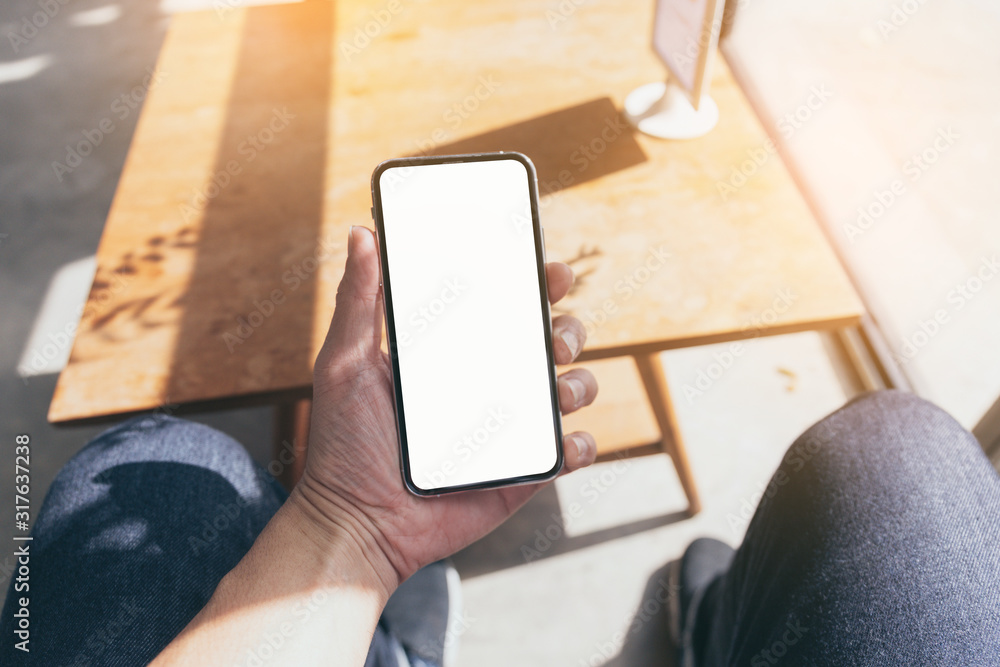 Wall mural mockup image blank white screen cell phone.man hand holding texting using mobile on desk at coffee s