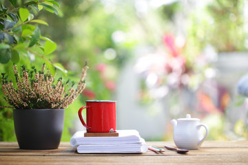 Red coffee cup with white tea pot and notebooks and heathers plants at outdoor