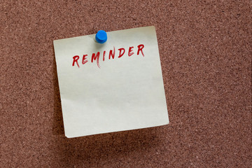 reminder written on a yellow memo note pinned to a memo board with a blue push pin