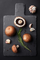 Fresh brown champignon with spices and herbs. Raw mushrooms on a black background. Top view