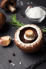 Fresh brown champignon with spices and herbs. Raw mushrooms on a black background