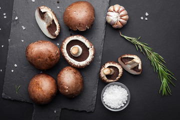 Fresh brown champignon with spices and herbs. Raw mushrooms on a black background. Top view