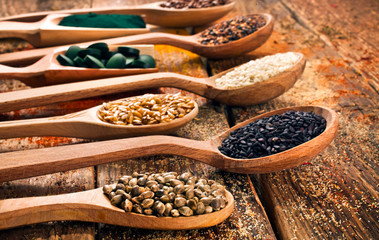 Nutritional supplement. Spirulina tablets and powder in the wooden scoops, linen seeds, cannabis seeds, sesame seeds on wooden background.