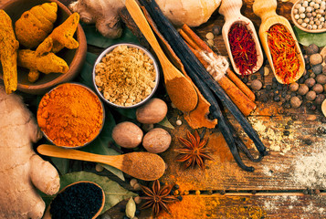Spices on wooden background. Different peppercorns, ginger, turmeric, saffron,  bay leaf, cloves, kalonji, nutmeg, anise, cinnamon and vanilla pods. Top view.