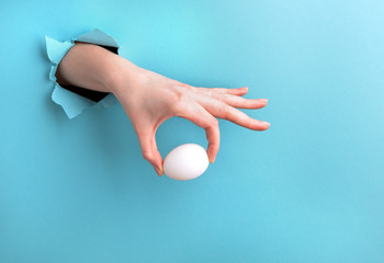 White egg in a woman's hand against a blue background with a hole