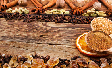 Ethnic ornament made of spices. Star anise, nutmeg, cardamom, cinnamon sticks, cloves, brown sugar with dried oranges, powder of cinnamon and sugar in spoons. Wooden background. Text space. 