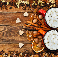 Sweet spices. Fluffy white marshmallows in enamel mugs with a variety of spices, dried orange slices, cinnamon sticks, cardamom, vanilla pod and nutmeg on wooden background. Text space. Top view.